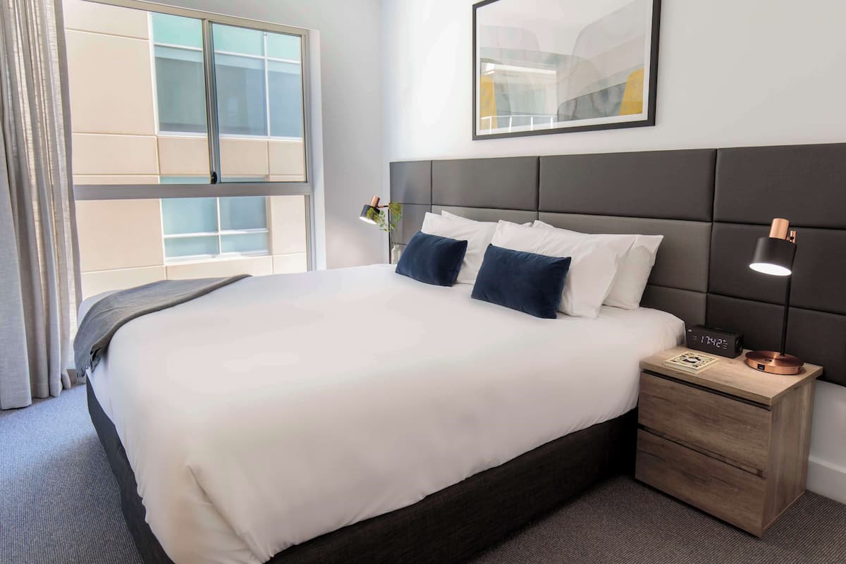 Een hotelkamer met een groot bed, een nachtkastje met een lamp en een raam met gordijnen.
