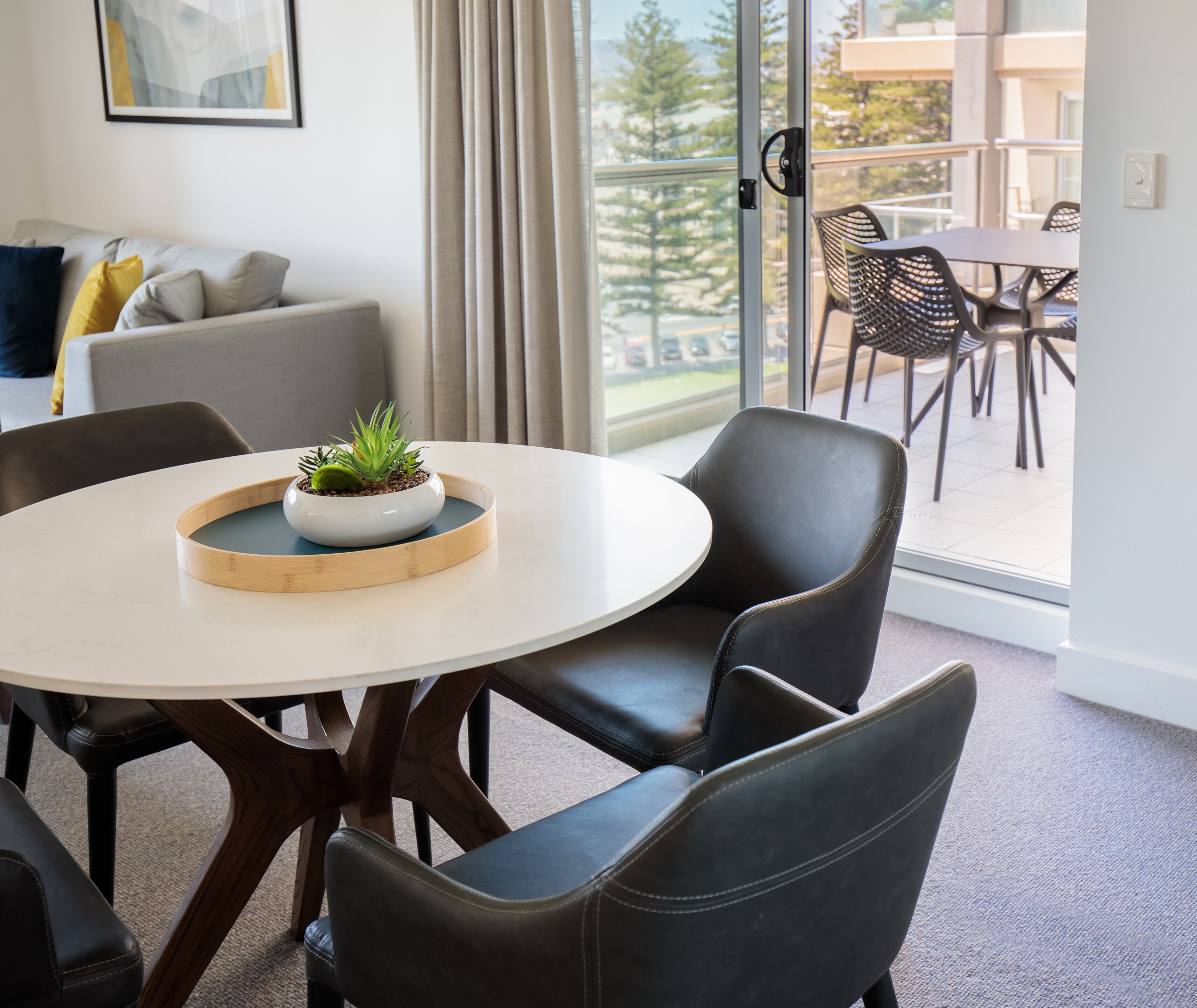 A modern dining area with a round table, black leather chairs, and a potted plant centerpiece.