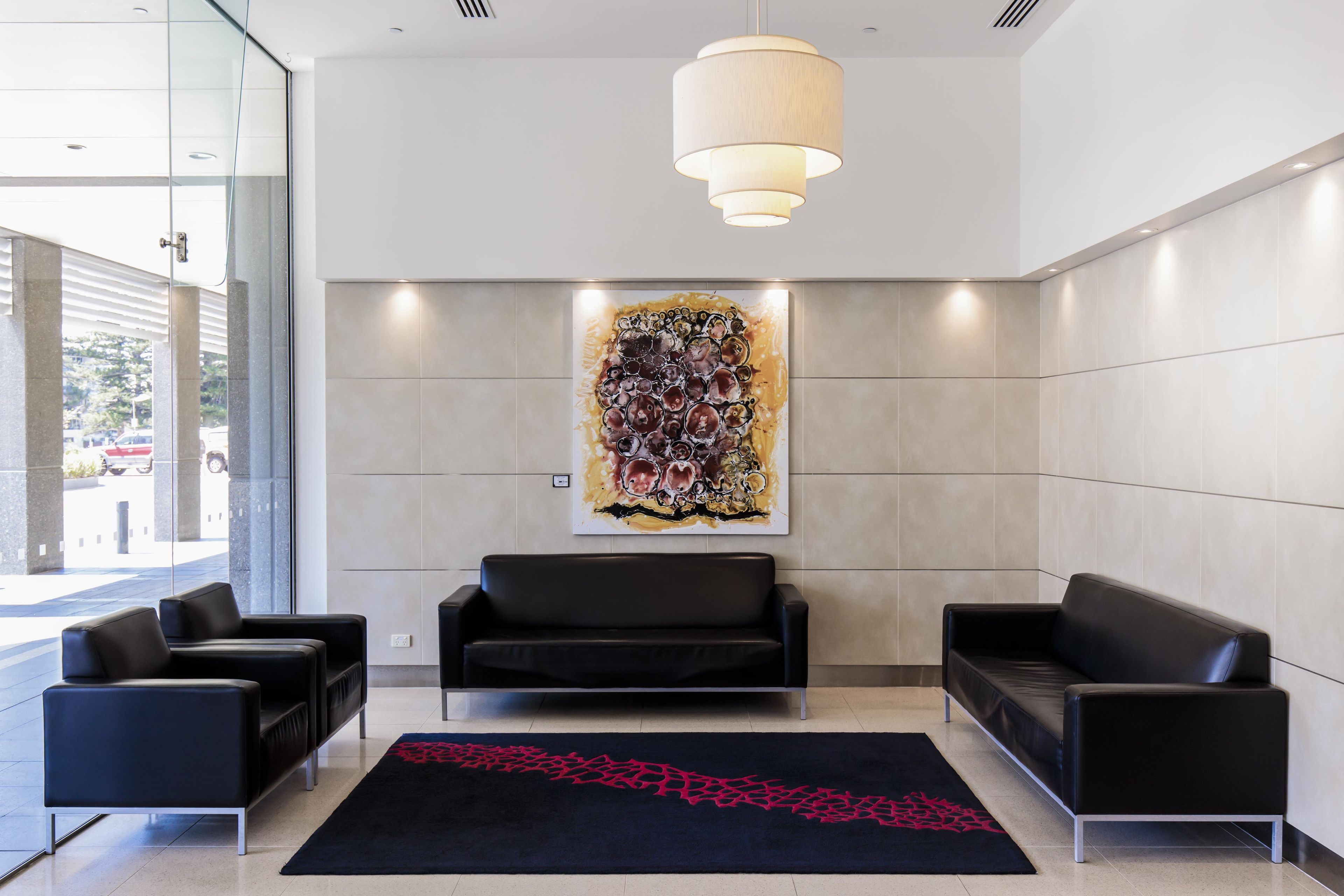 A modern lobby with black leather sofas, a large abstract painting, and a black rug with red patterns.