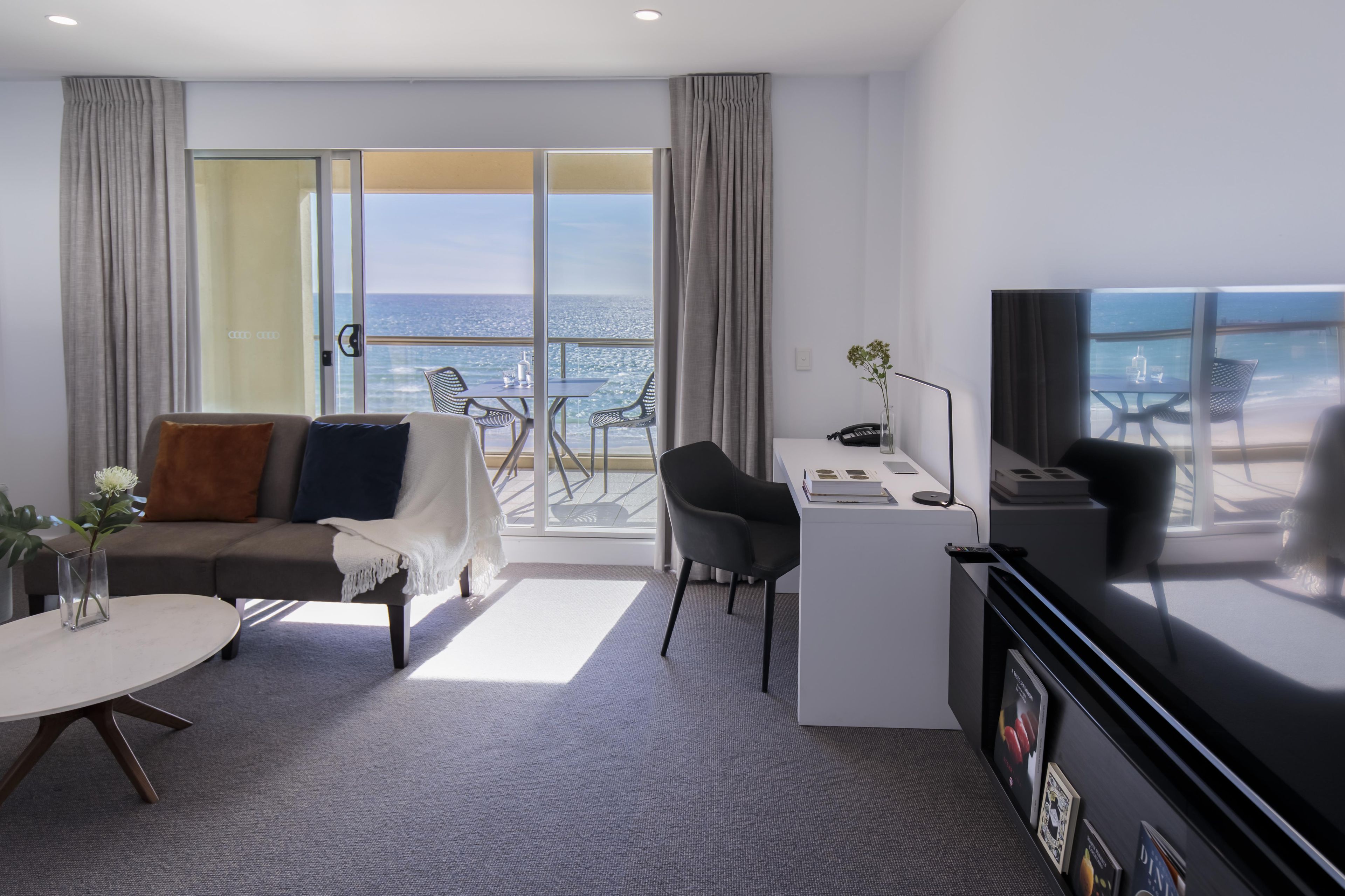 Habitación de hotel moderna con sofá, escritorio, televisión y vista al océano.