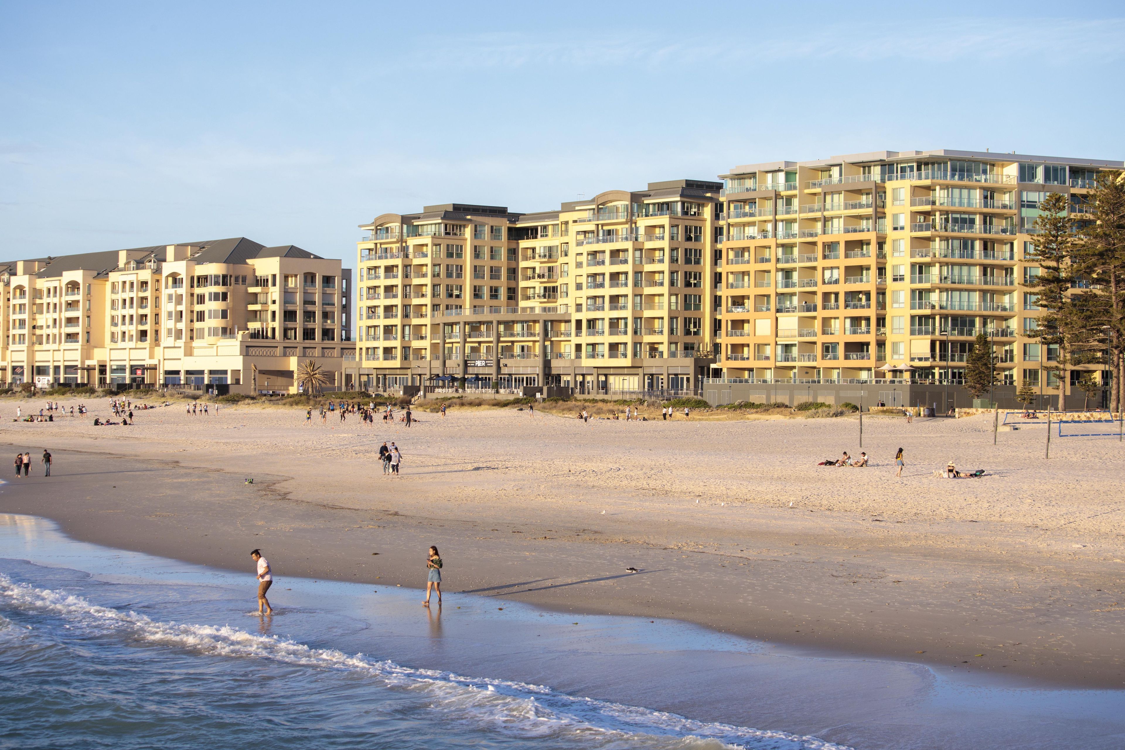 A beachfront hotel with multiple floors, balconies, and a sandy beach in the foreground.