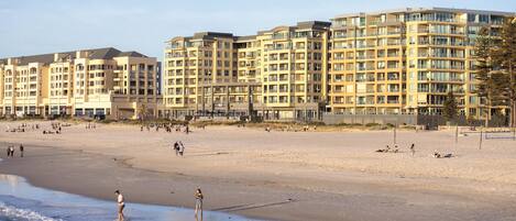 A beachfront hotel with multiple floors, balconies, and a sandy beach in the foreground.