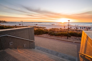 A beach with a pier extending into the water, a staircase leading down to the beach, and a clear sky. - Oaks Glenelg Plaza Pier Suites (Glenelg)