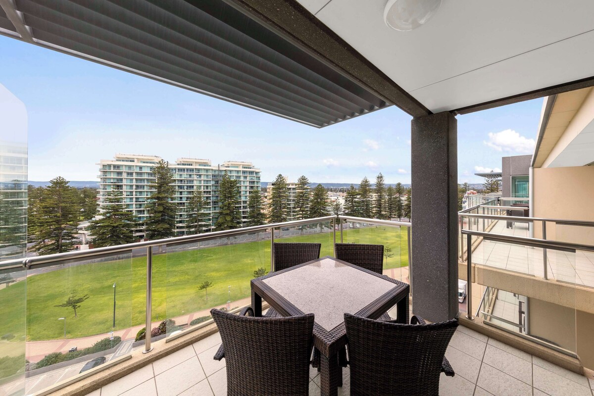 Un balcon avec une table et des chaises, d’où l’on peut admirer une pelouse et des bâtiments situés au loin.