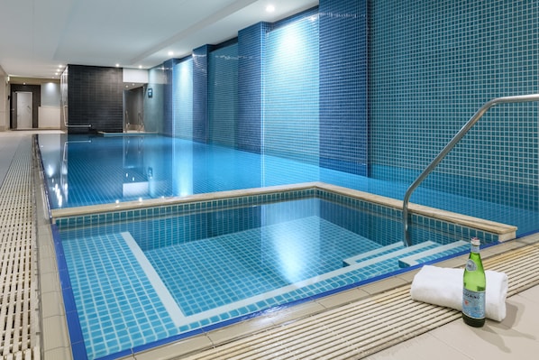 A swimming pool with blue tiles, a metal ladder, and a bottle of beer on the edge.