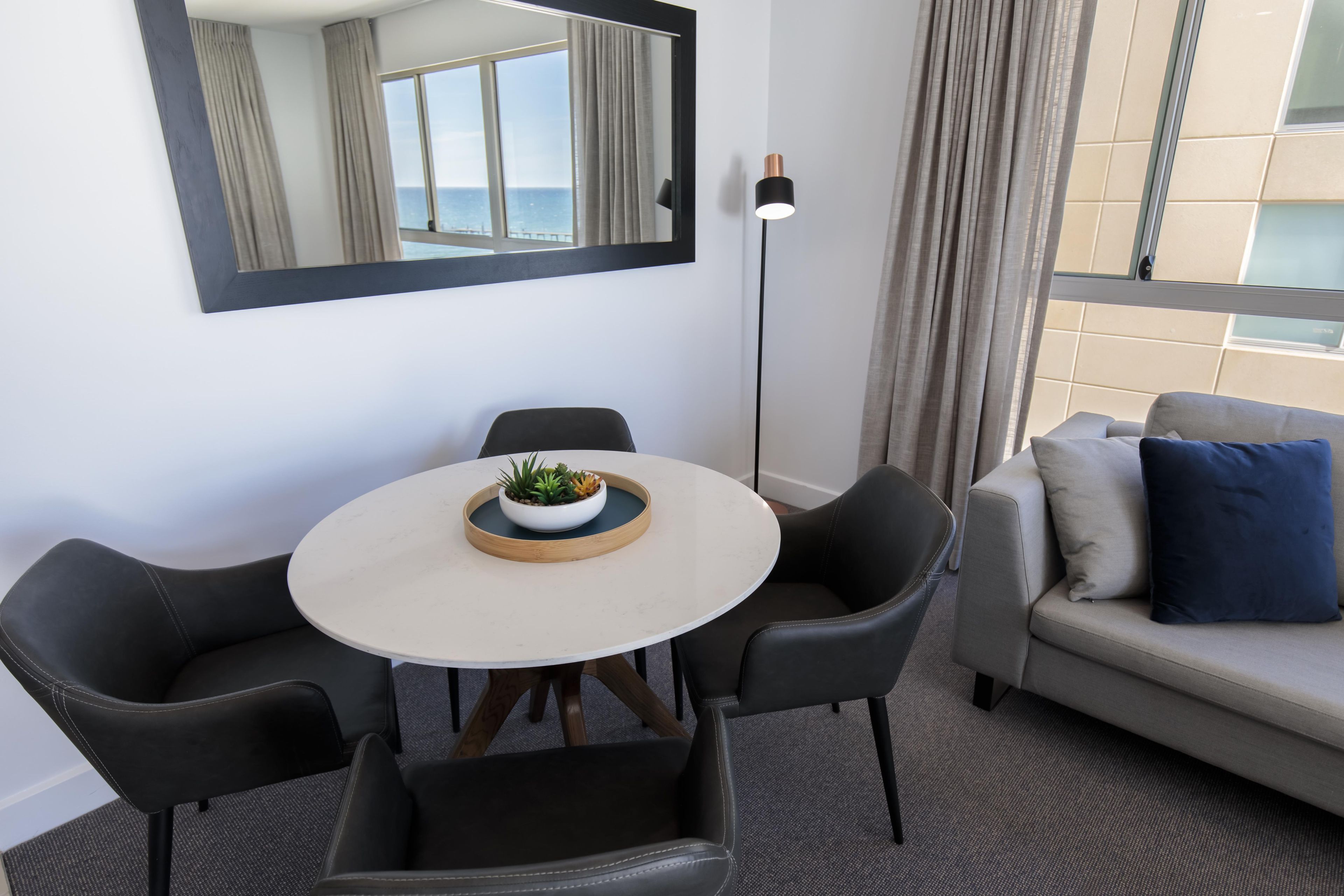 Une pièce moderne avec une table ronde, deux chaises, un canapé, un lampadaire et un grand miroir.