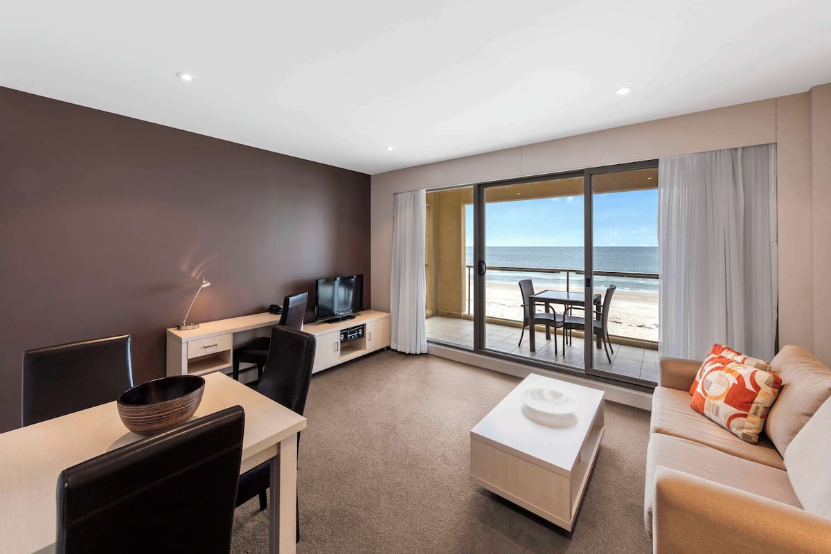 Een moderne hotelkamer met een zithoek, een televisie en een groot raam met uitzicht op het strand.