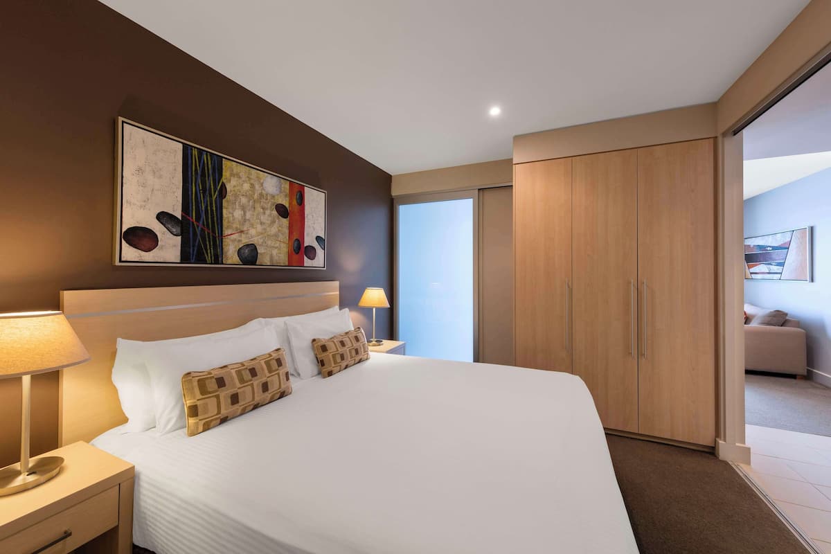 Een moderne hotelkamer met een groot bed, een nachtkastje met lamp, een garderobe en een schilderij aan de muur.