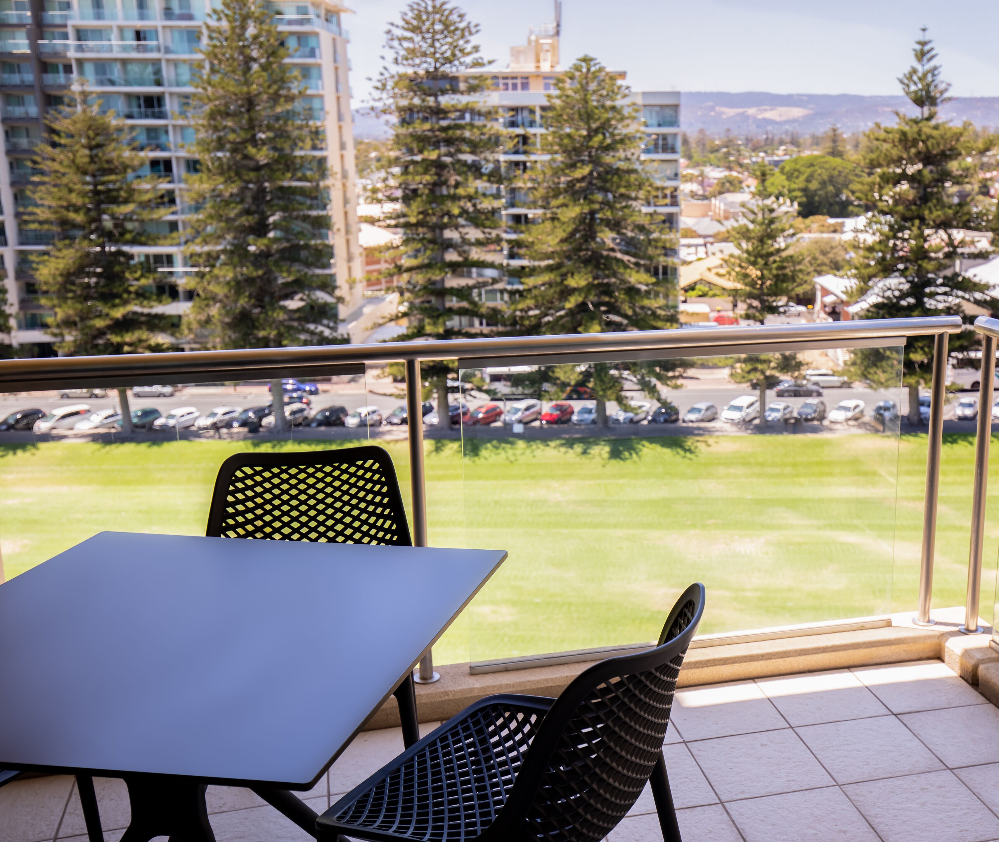 Un balcon avec une table et des chaises, donnant sur un parking et des immeubles.