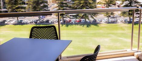 Un balcon avec une table et des chaises, donnant sur un parking et des immeubles.