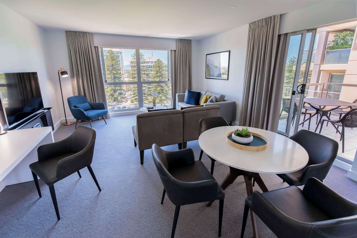 Een moderne hotelkamer met een groot raam, een bank, een eettafel met stoelen en een televisie.