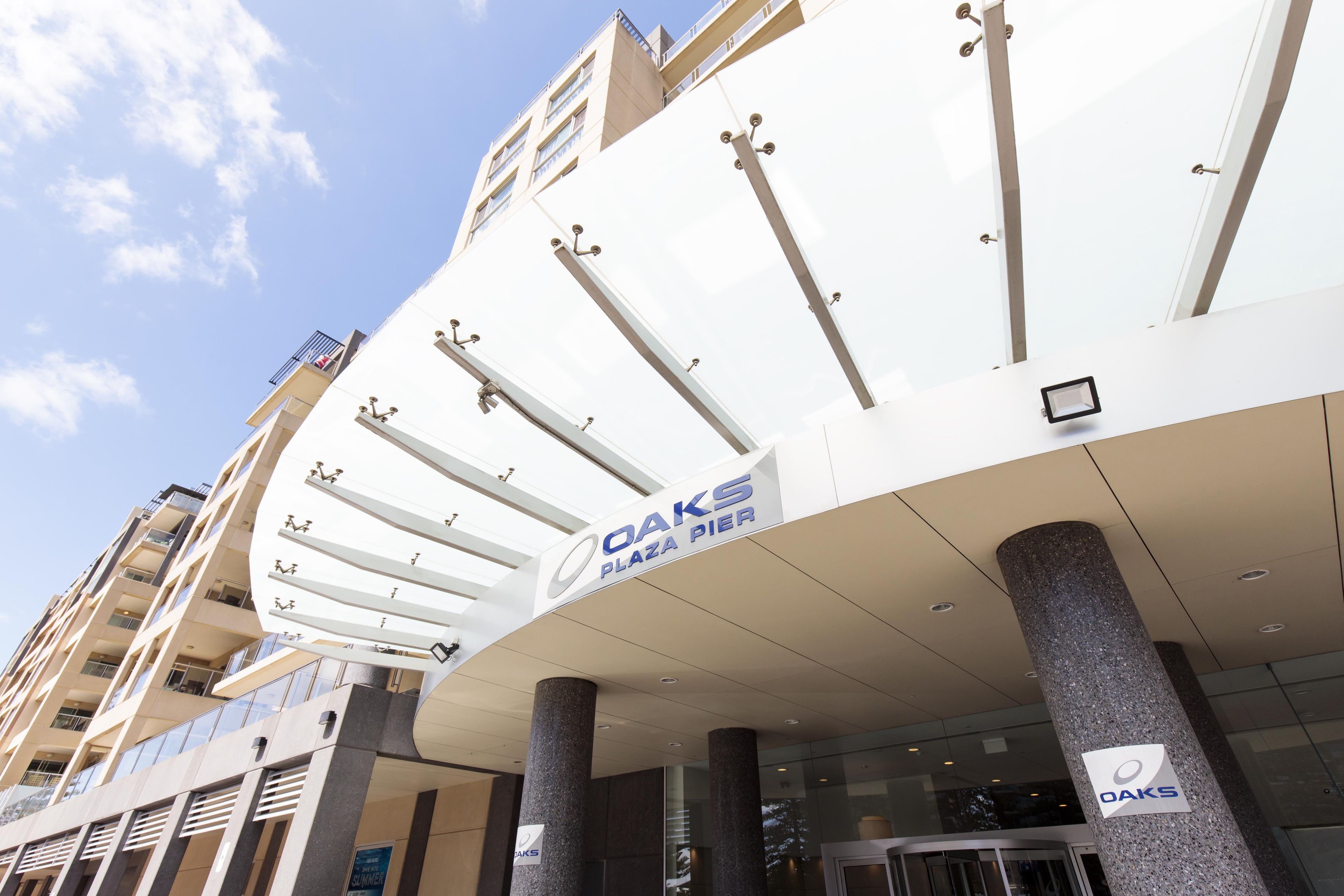 A modern building with a prominent 'OAKS PLAZA PIER' sign, multiple balconies, and a glass entrance.
