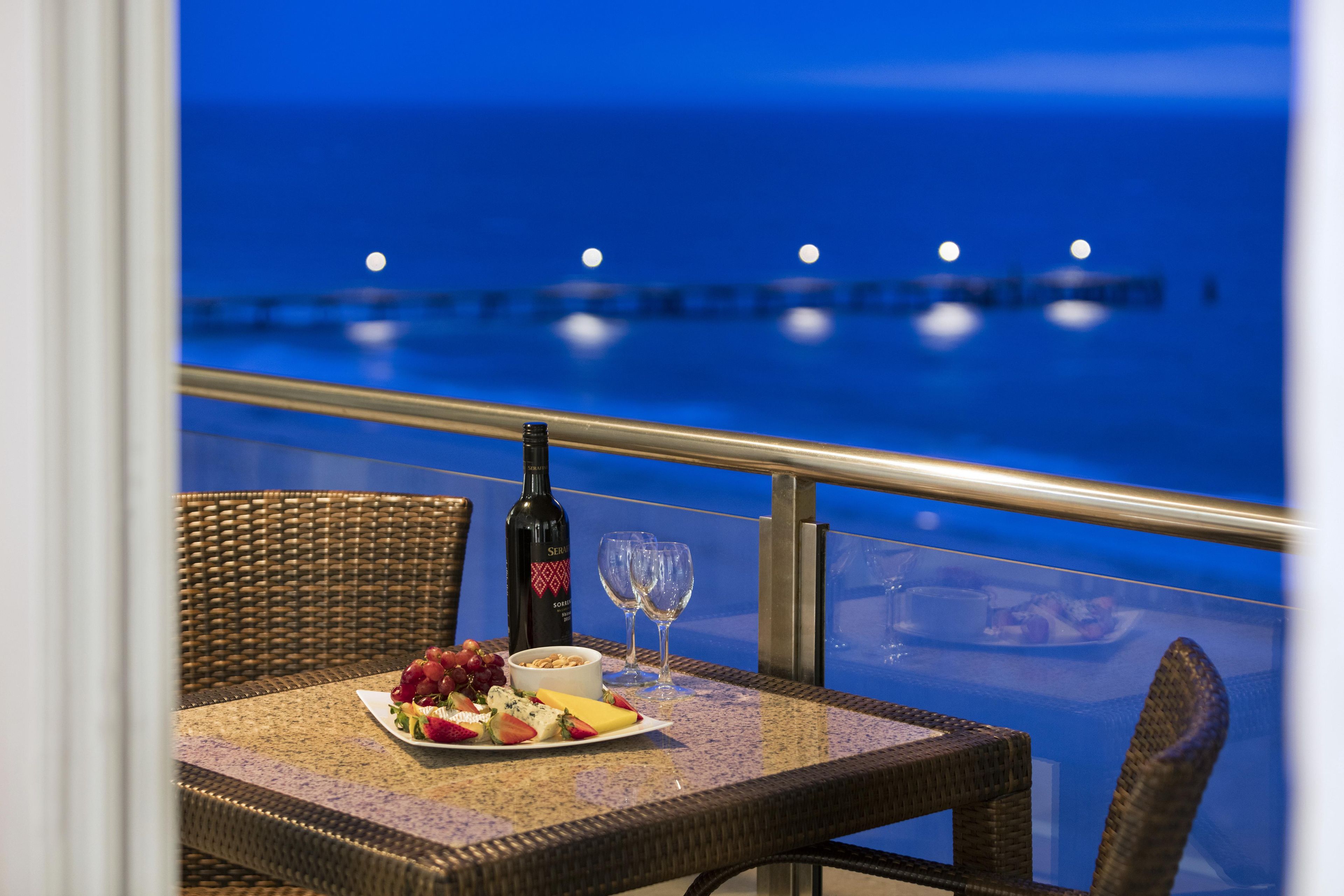 A dining table with a bottle of wine, glasses, and a plate of fruit and cheese.
