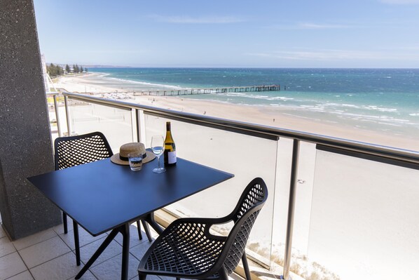 A balcony with a table and chairs overlooking a beach with a pier.