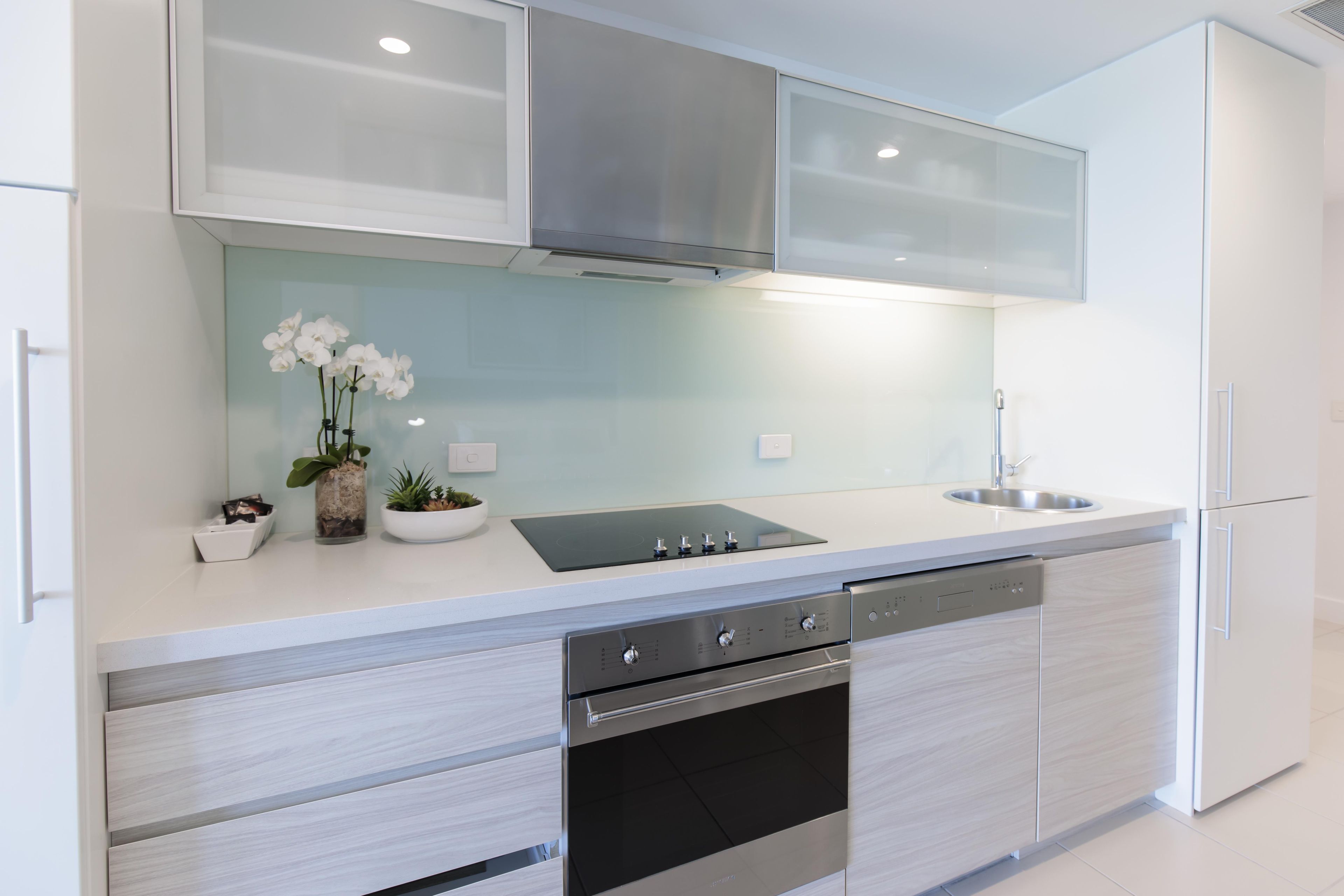 A modern kitchen with a built-in oven, a stainless steel sink, and a double-door refrigerator.