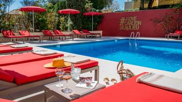 A poolside area with red lounge chairs, a table with drinks, and a wall with a message.
