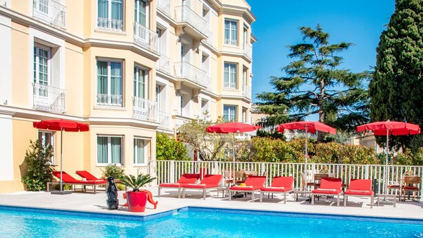 Ein Hotelpoolbereich mit roten Liegestühlen, einem Glastisch mit Flasche und Buch sowie einem klaren, blauen Pool.