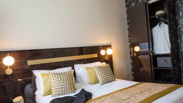 A hotel room with a large bed, a wardrobe with a mirror, and a nightstand with a lamp.