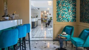 Eine moderne Hotellobby mit Marmorboden, einer Bar mit blauen Stühlen, Petrol-Armlehnstühlen und einer großen Blumenwand.