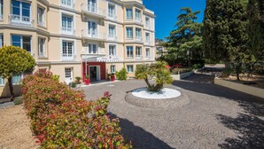 Ein mehrstöckiges Hotel mit Innenhof, rotem Eingang und umgebender Bepflanzung.