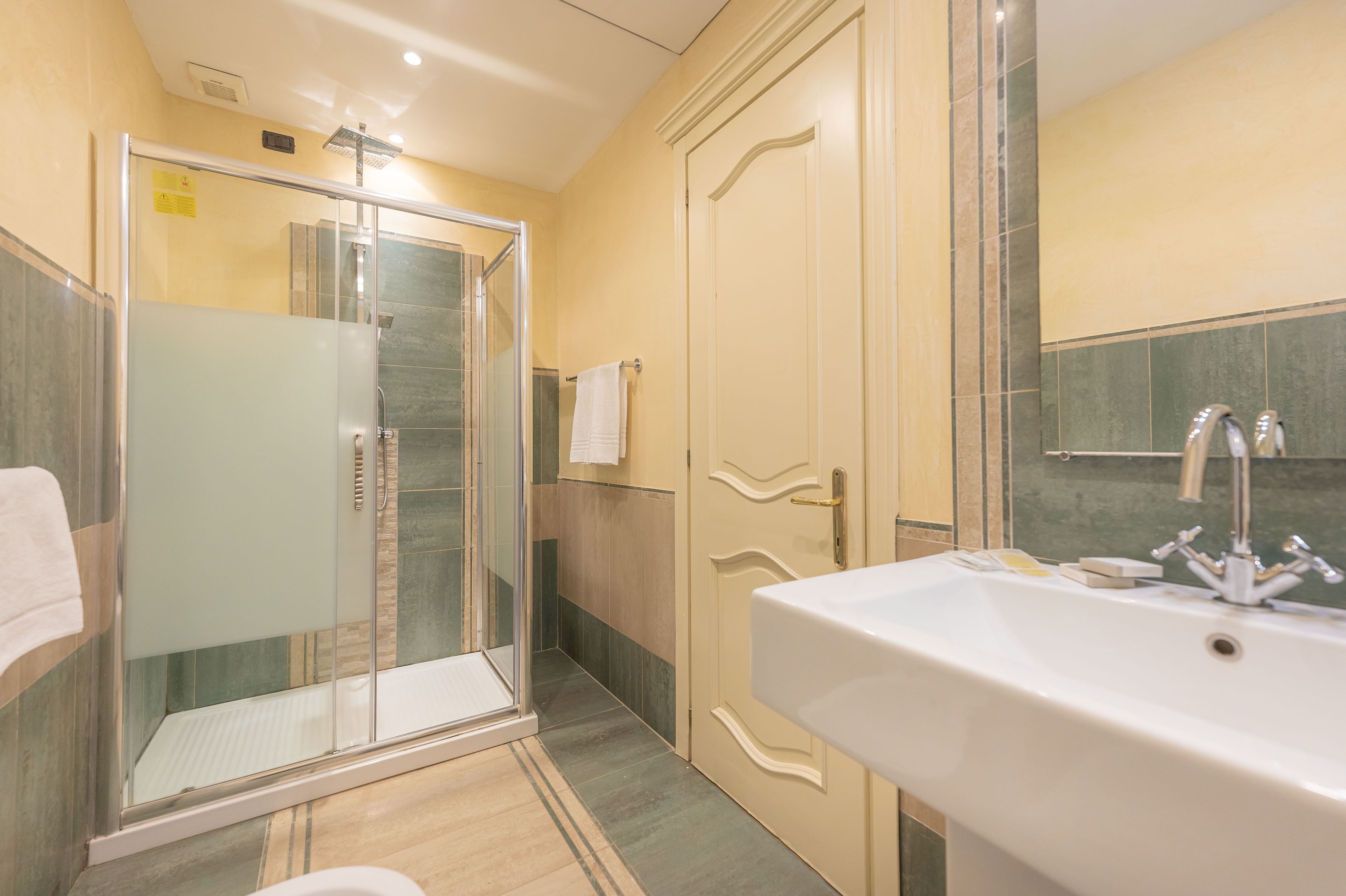 Un bany amb dutxa de vidre, un lavabo amb mirall i un escurapulides.
