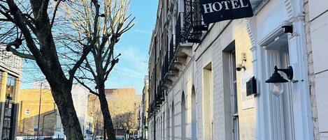 Une rangée de bâtiments traditionnels en briques, avec une enseigne indiquant « Arriva Hotel » à l’angle.