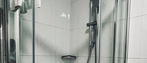 A glass-enclosed shower stall with a handheld showerhead and a handheld shower attachment.