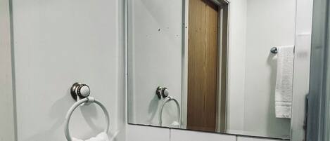 Casa de banho com lavatório branco, suporte de toalha, espelho e toalha pendurada na parede.