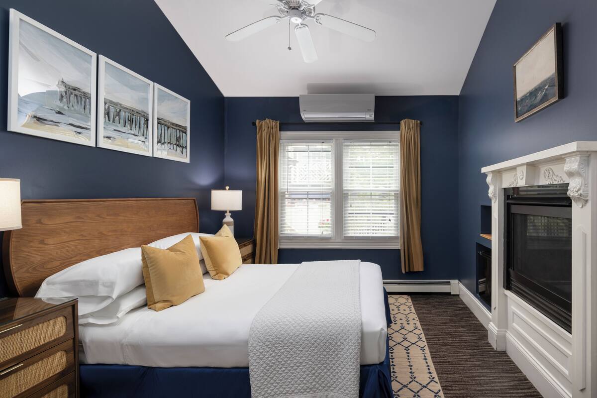A hotel room with a large bed, a wooden headboard, a fireplace, and a window with curtains.