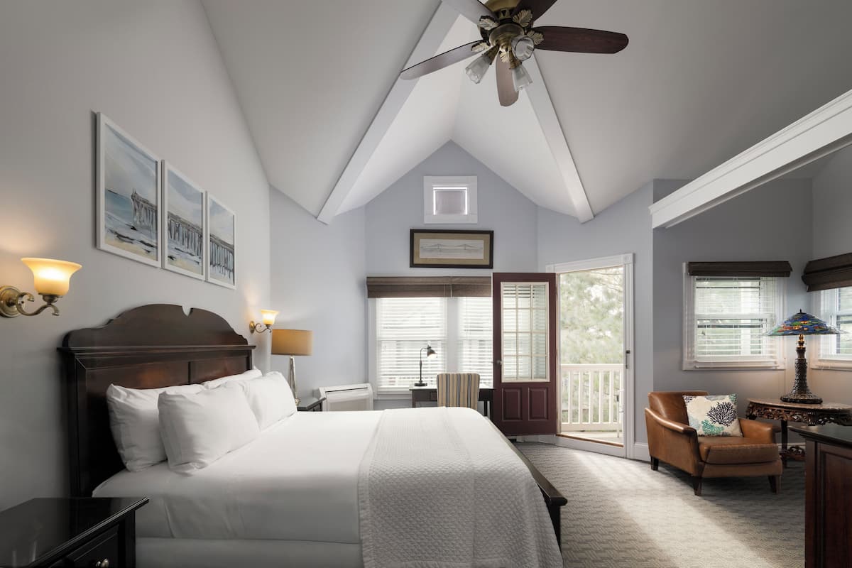 A bedroom with a large bed, a ceiling fan, a desk with a lamp, and a chair.