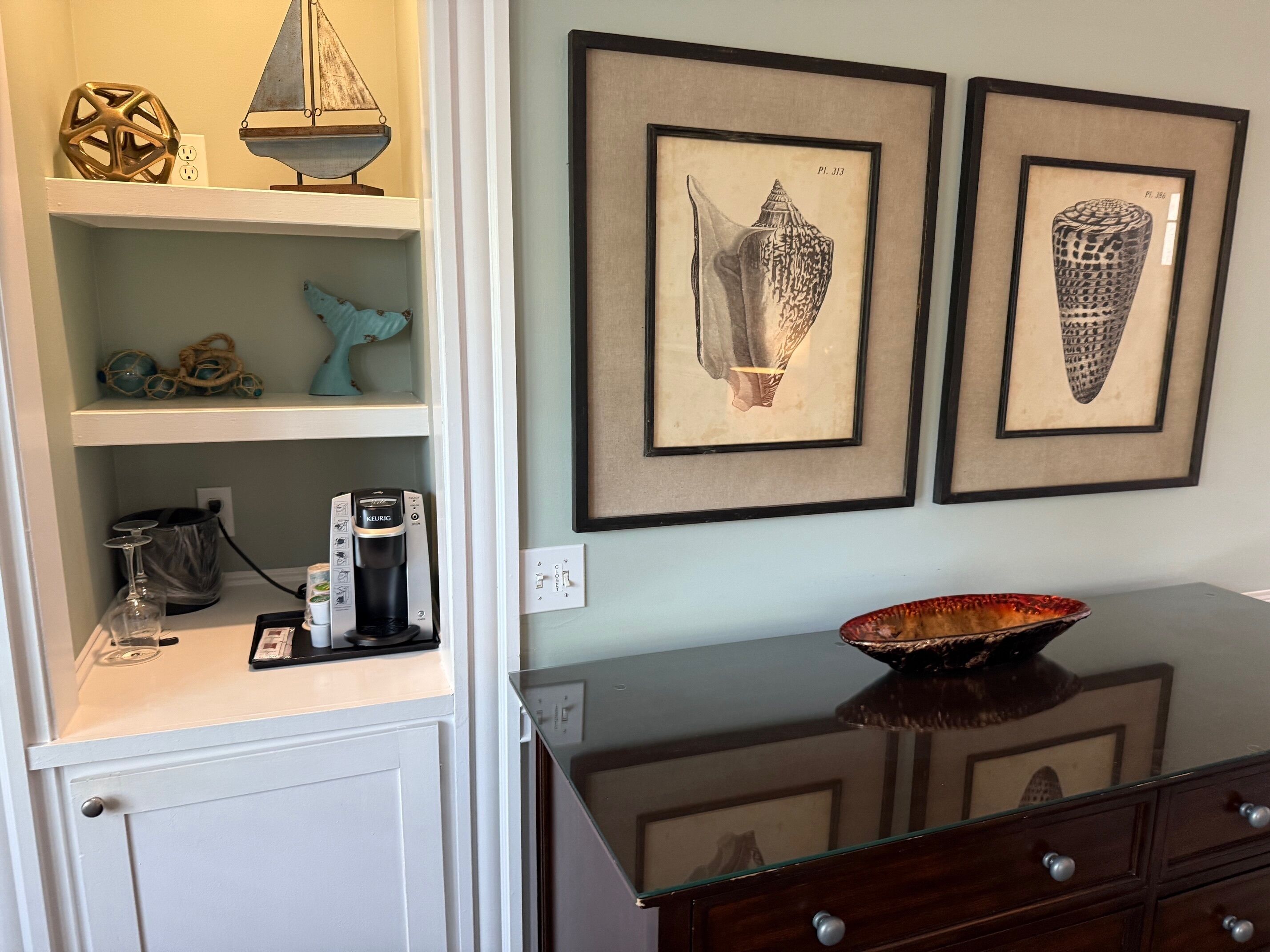 A room with a white cabinet, a coffee maker, and two framed pictures on the wall.