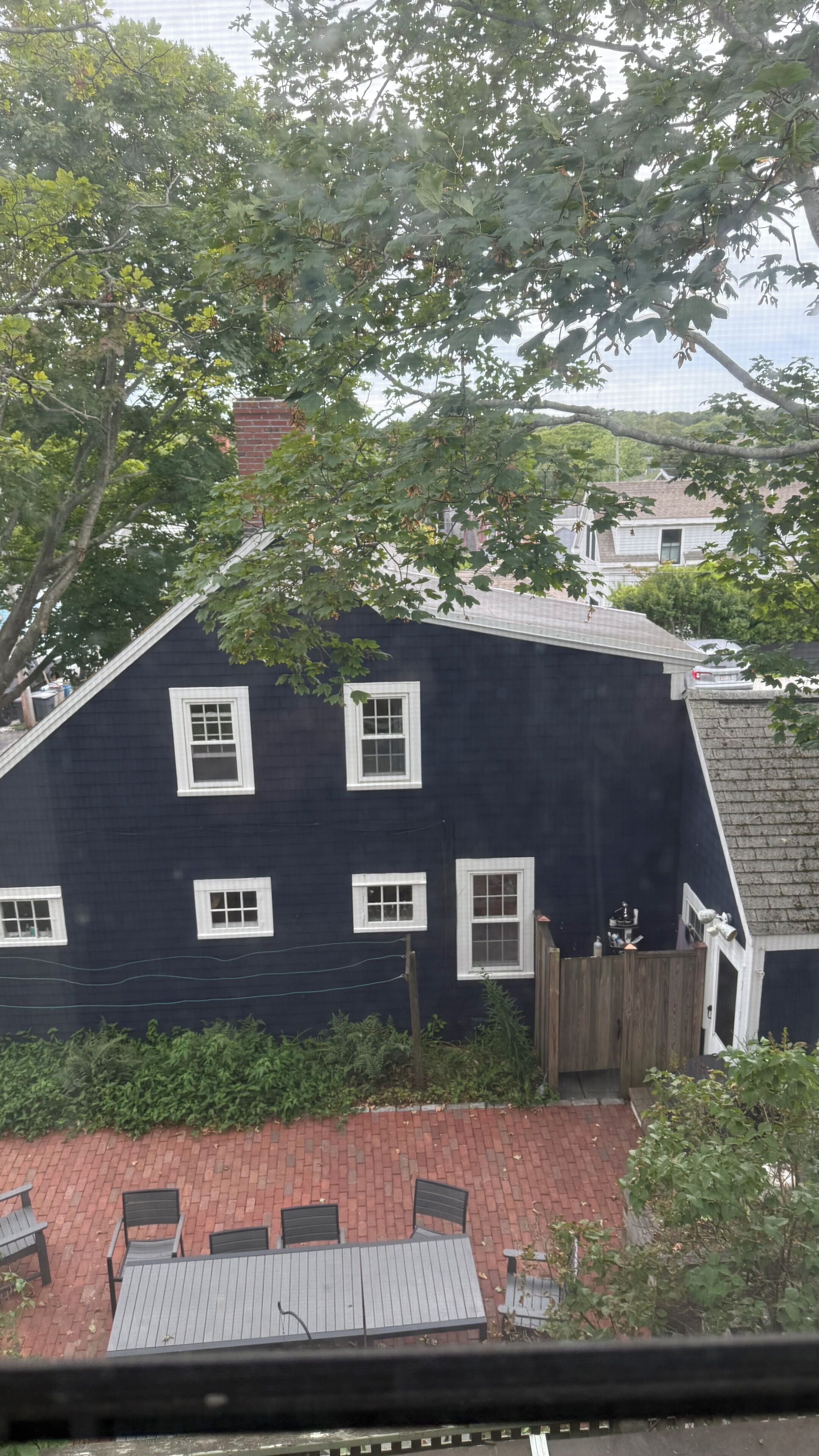 Uma casa de cor escura com três janelas e um alpendre de tijolos com móveis de exterior.
