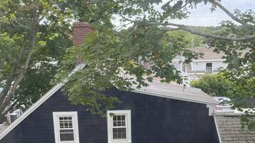 Uma casa de cor escura com três janelas e um alpendre de tijolos com móveis de exterior.