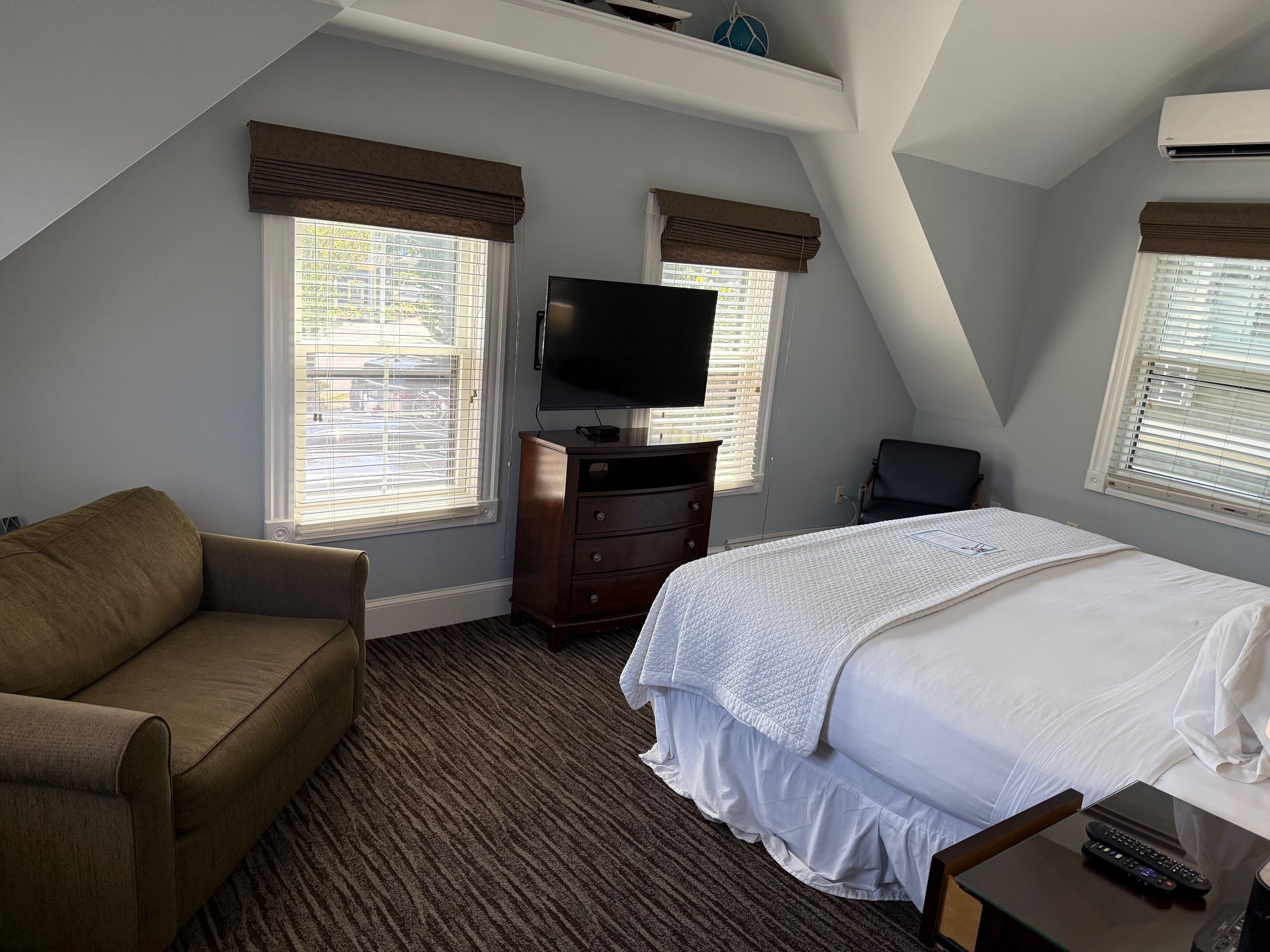 A hotel room with a bed, a TV, a dresser, a chair, and a window with blinds.