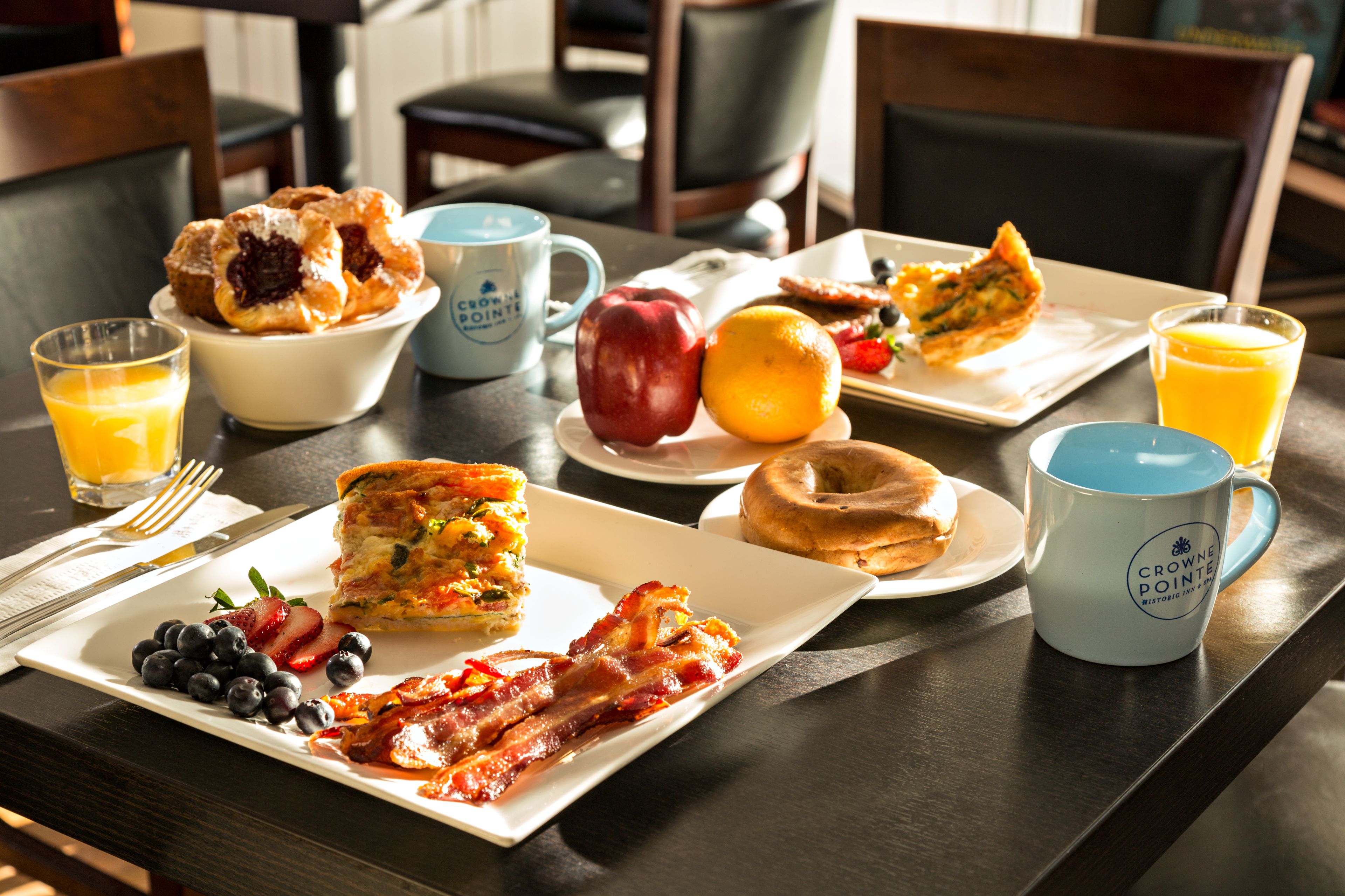 Mesa de café da manhã com diversos alimentos, incluindo ovos, bacon, frutas e uma xícara de café.