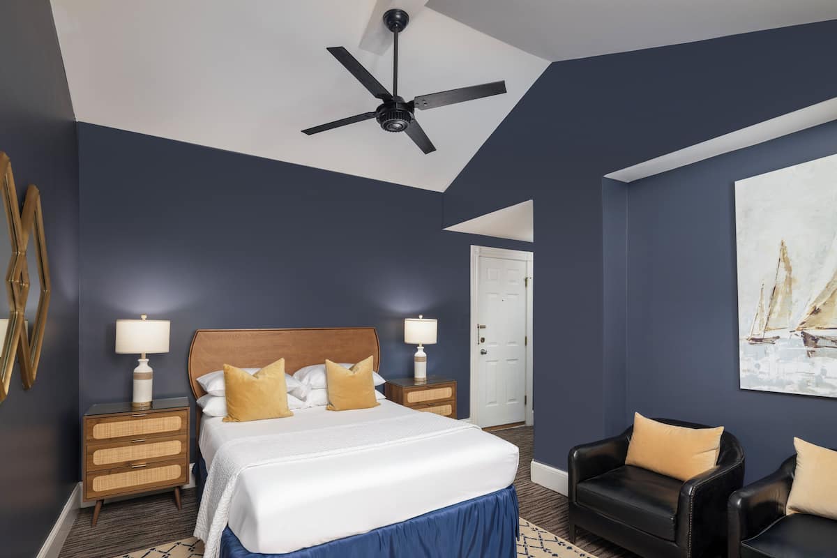 A bedroom with a bed, two nightstands, a ceiling fan, a door, and a painting on the wall.
