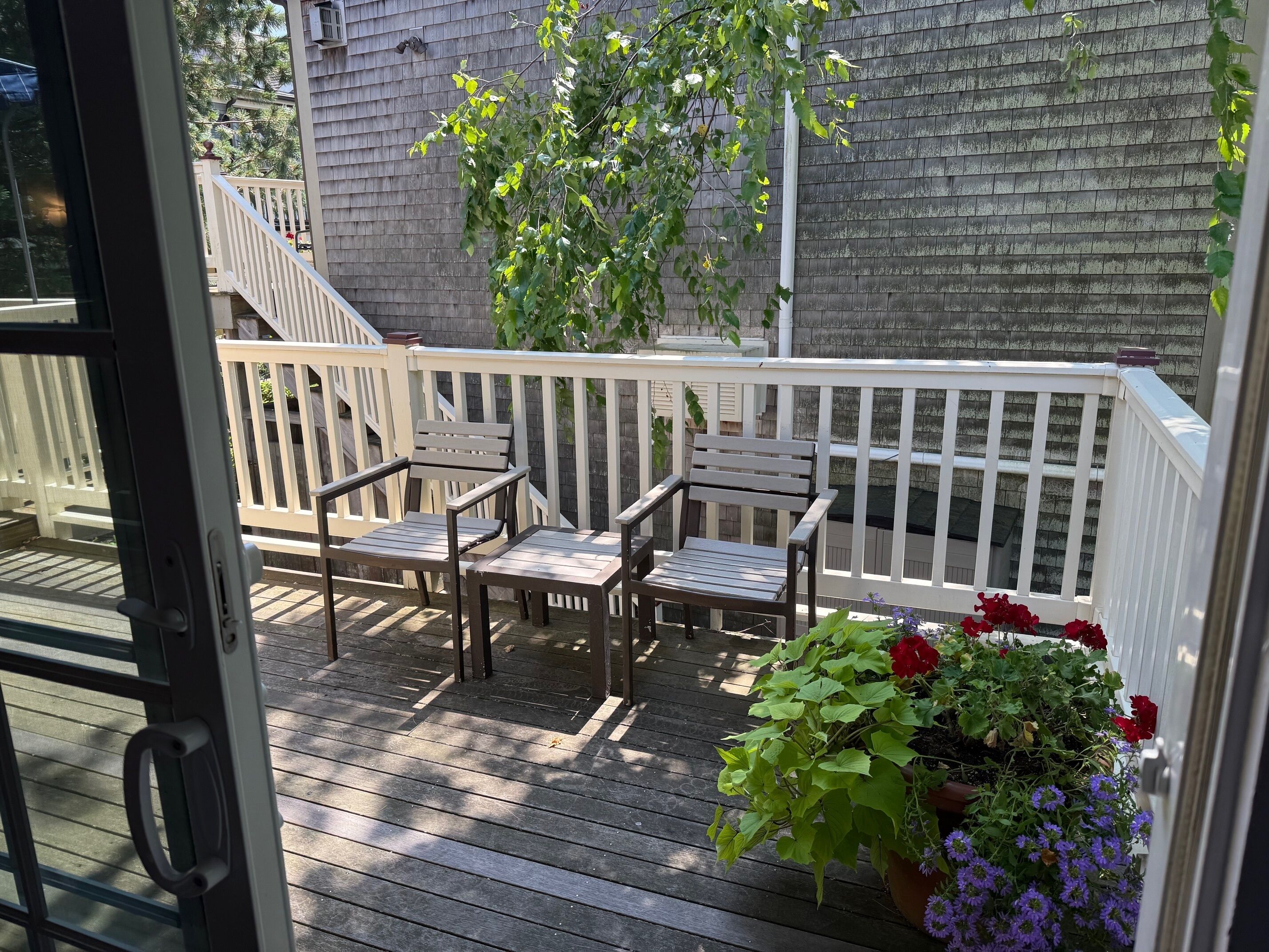 Een houten terras met twee stoelen en een potplant met rode en paarse bloemen.