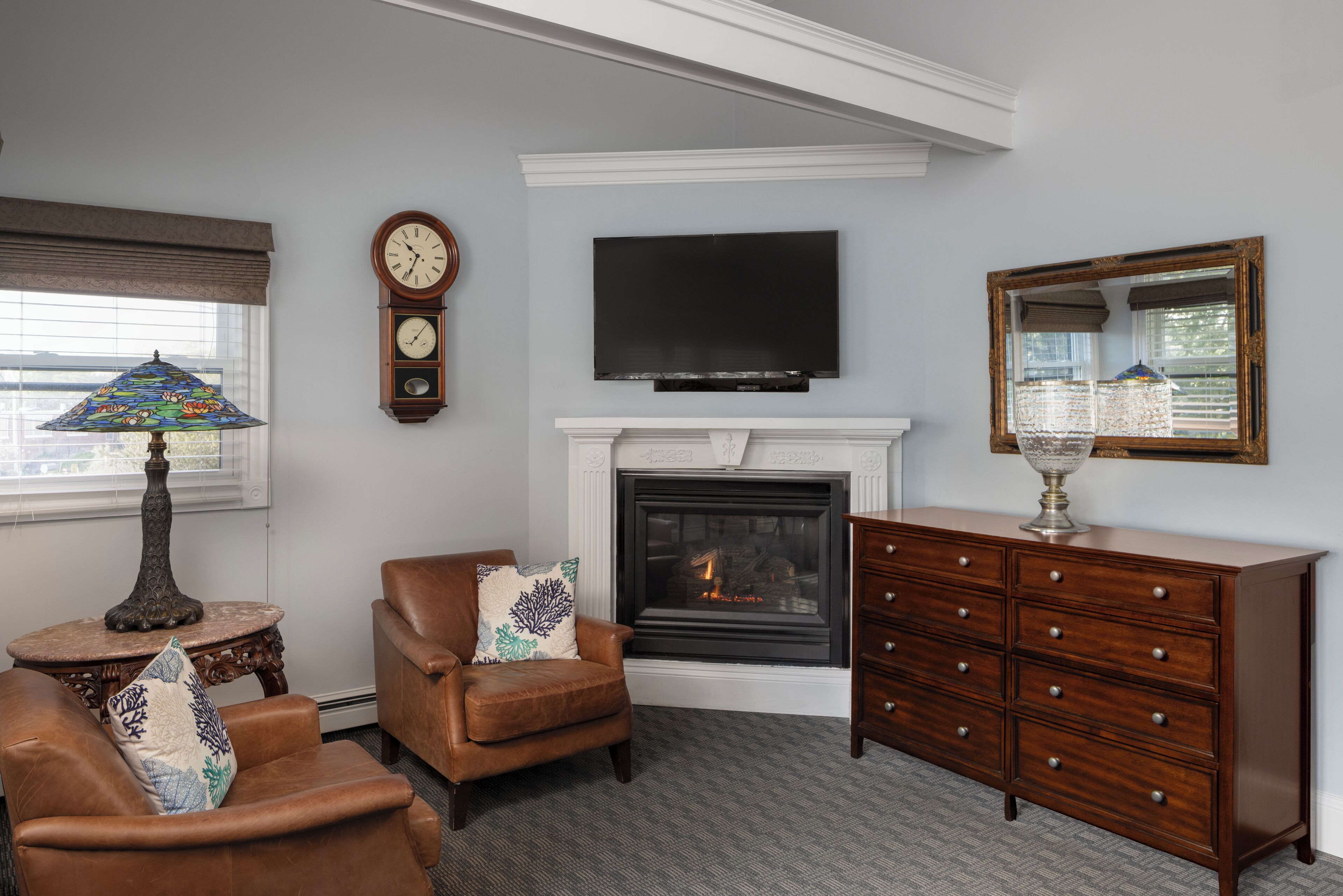 A living room with a fireplace, a television, a clock, and a mirror.