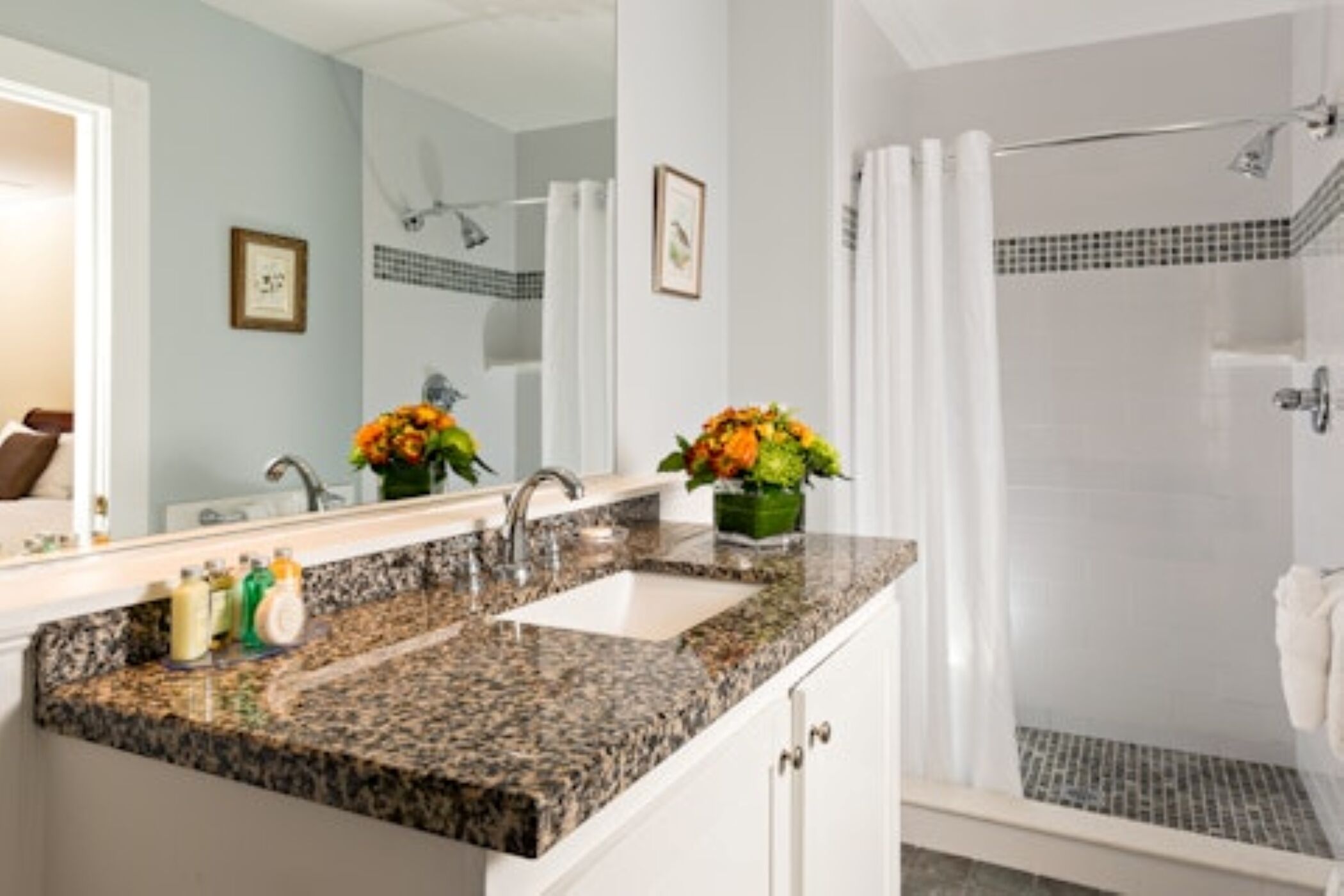 A bathroom with a granite countertop sink, a shower with a glass door, and a mirror above the sink.