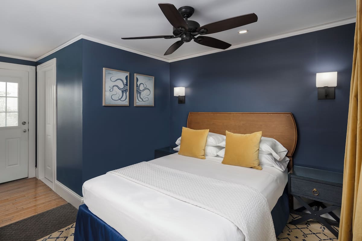 A bedroom with a bed, ceiling fan, wall-mounted lights, and artwork.