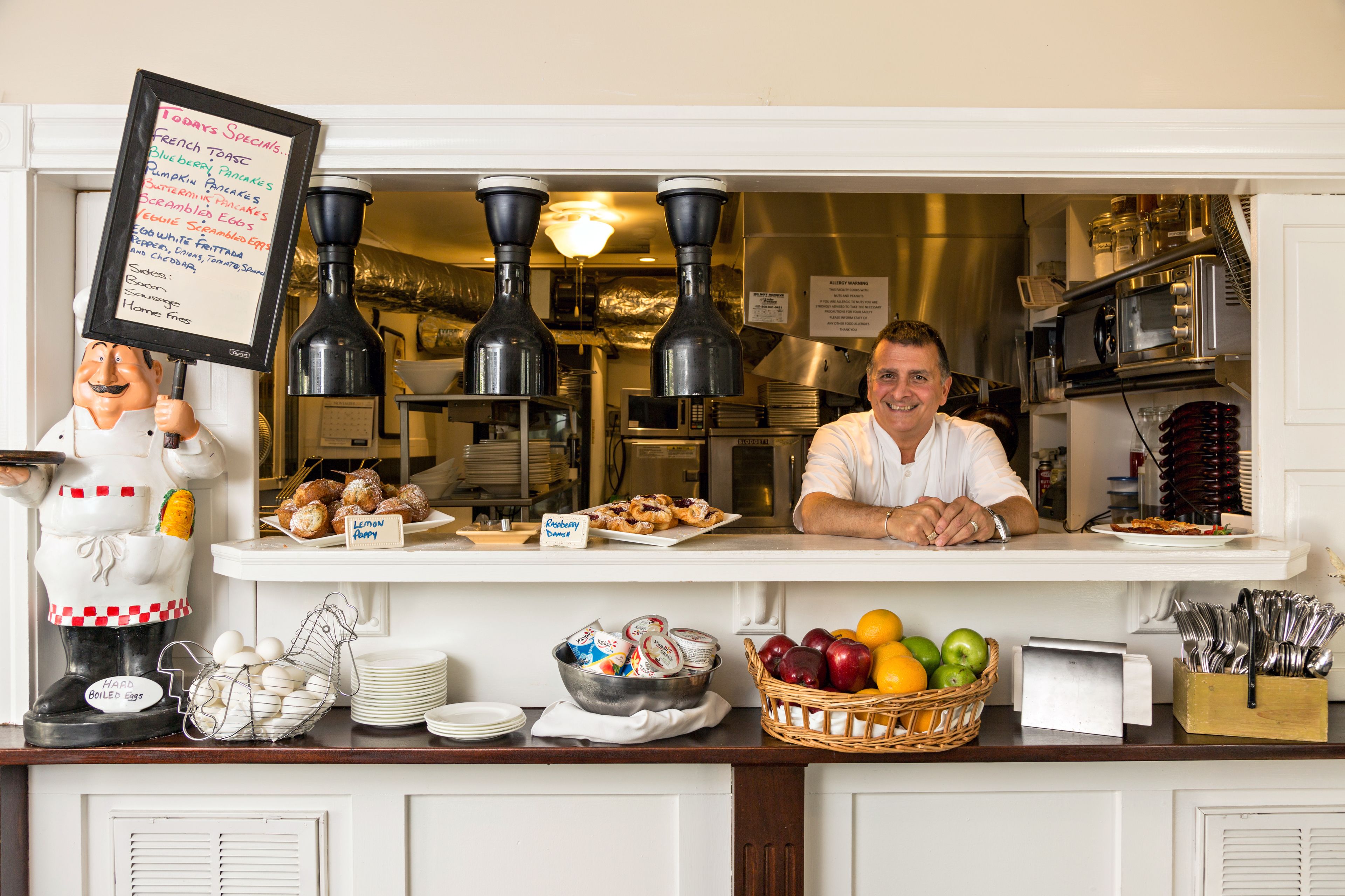 Una barra de desayuno con un panel de menú, una figura de chef y diversos alimentos para el desayuno.