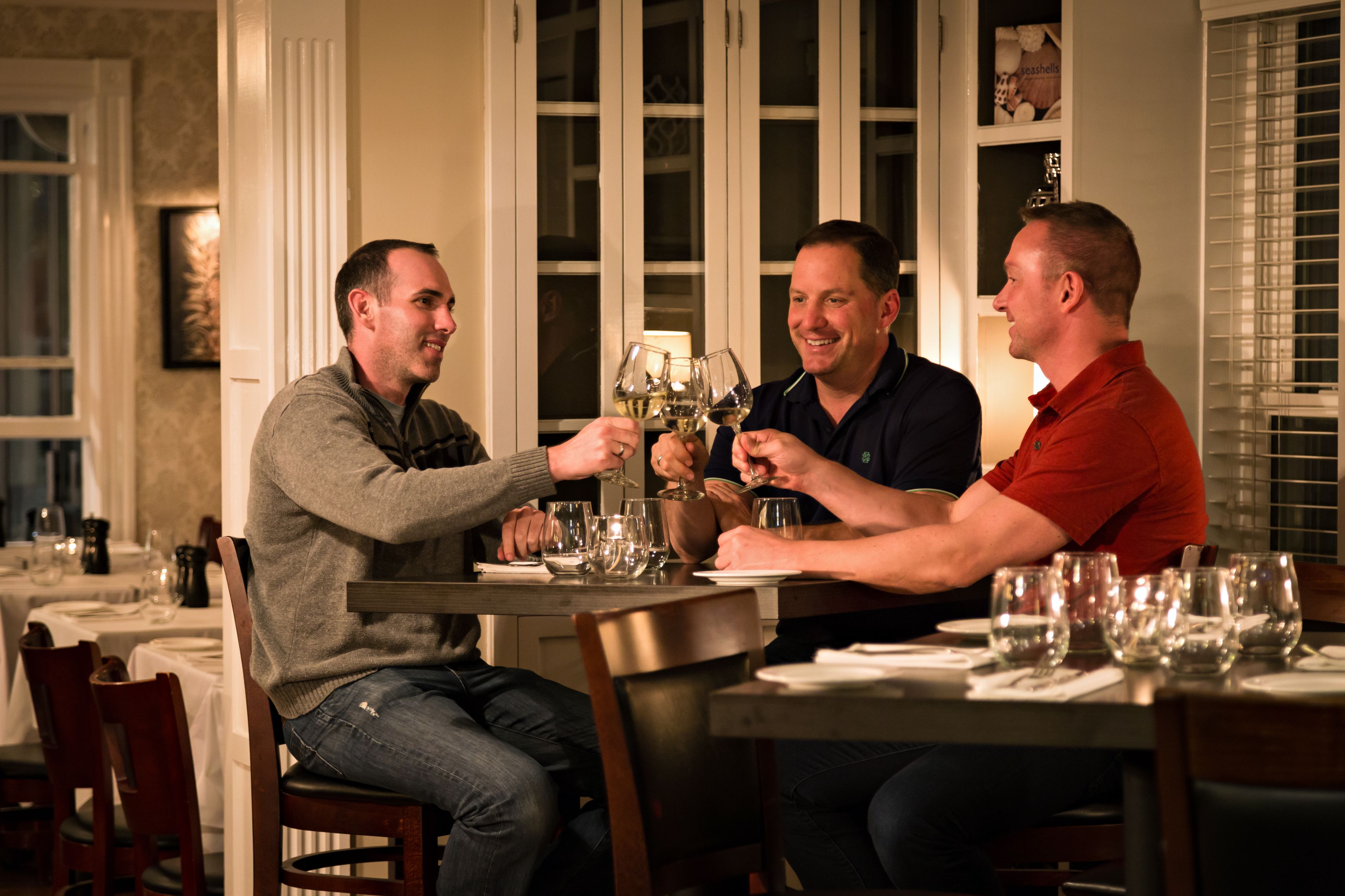 Una mesa de comedor con tres personas brindando con copas de vino.