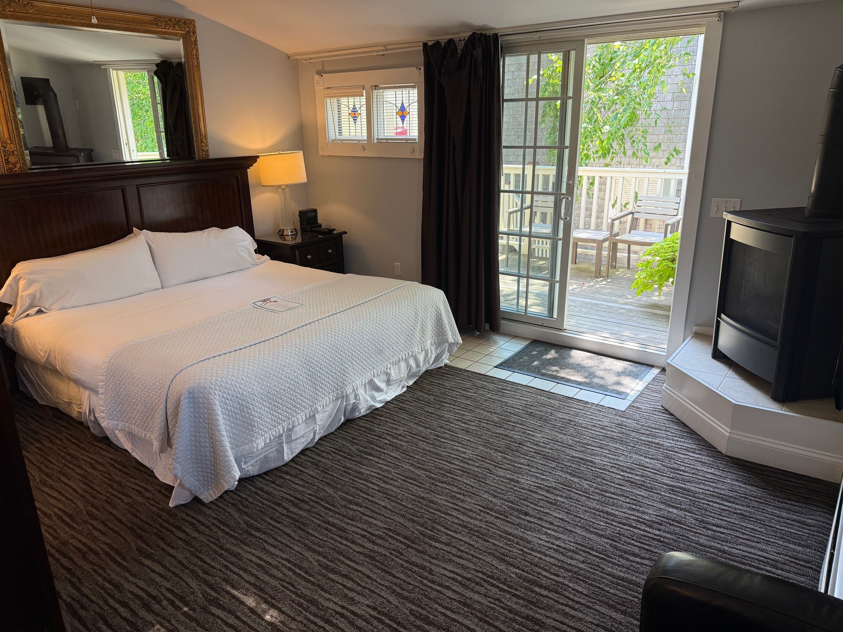 A hotel room with a bed, a TV, a nightstand, a lamp, a window with curtains, and a view of the outdoors.