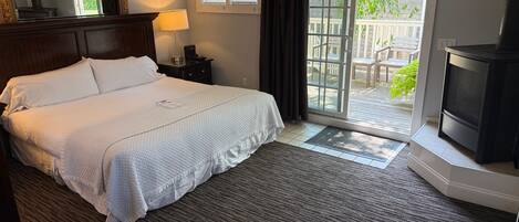A hotel room with a bed, a TV, a nightstand, a lamp, a window with curtains, and a view of the outdoors.