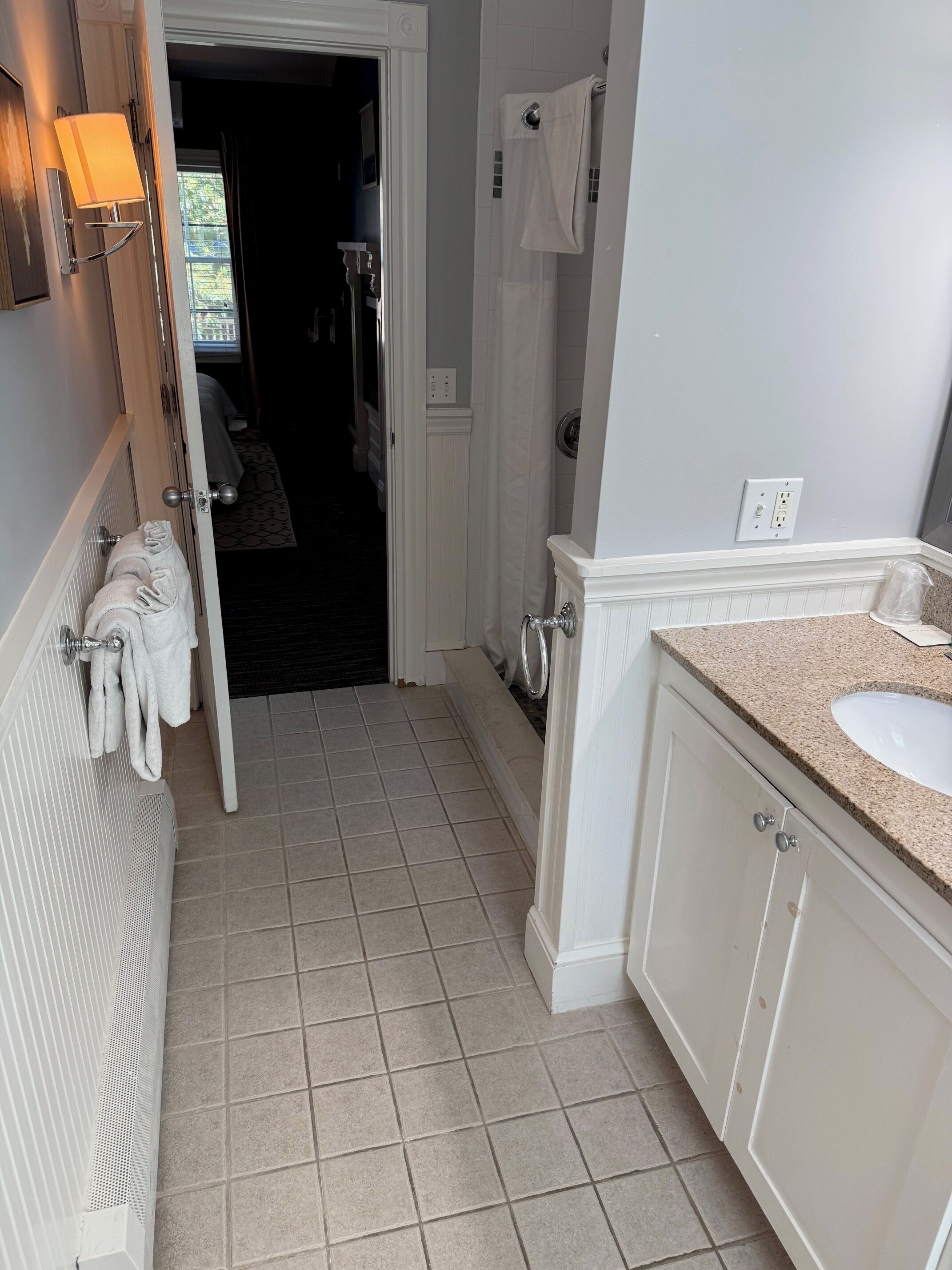A bathroom with a sink, mirror, towel rack, and a door leading to a bedroom.
