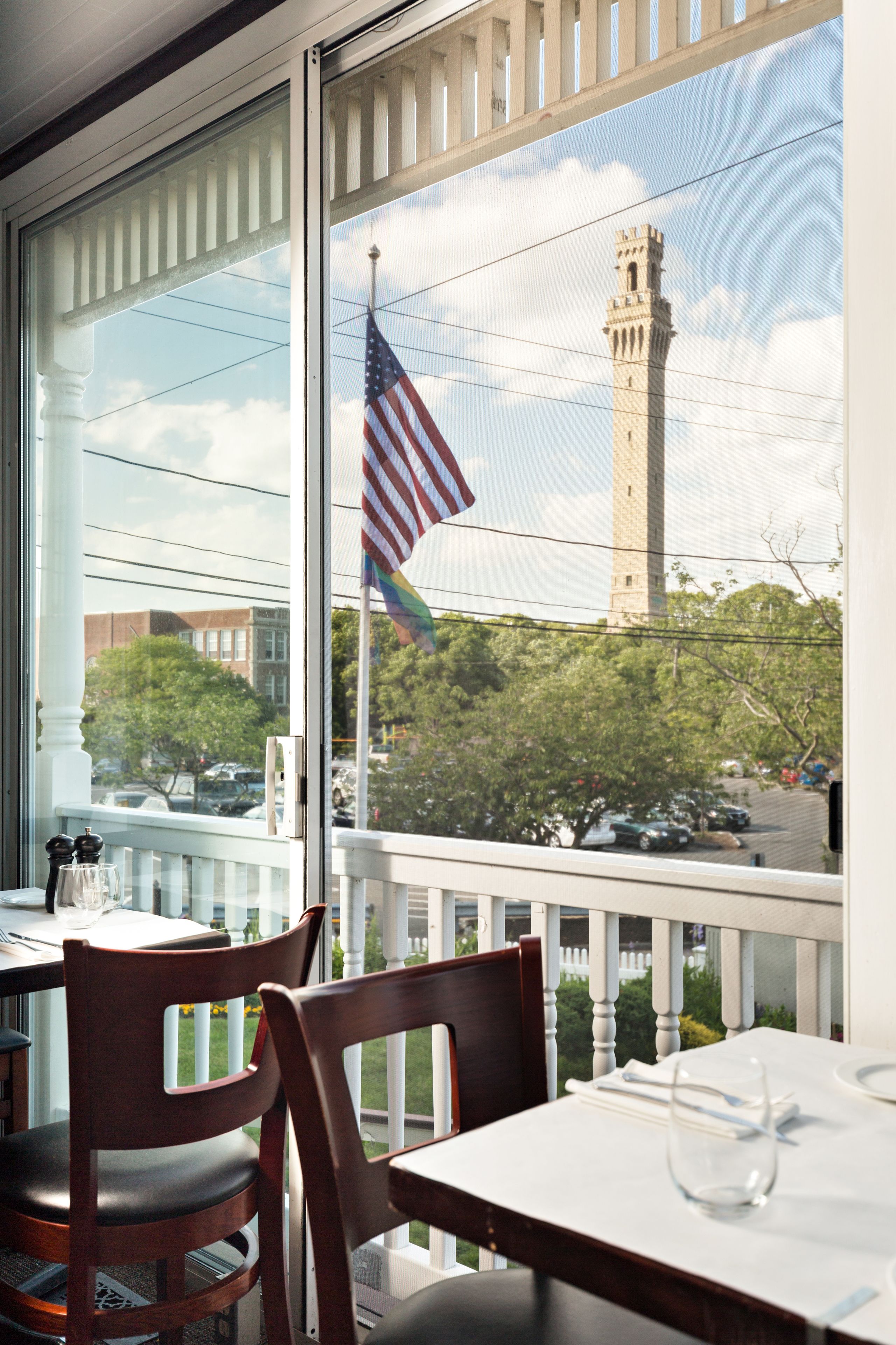 A dining area with a table and chairs, a window with a view of a tower and flag, and a white railing.