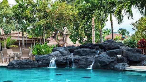 A pool with a waterfall feature surrounded by palm trees and lounge chairs. - Waikoloa Colony Villas (Waikoloa)