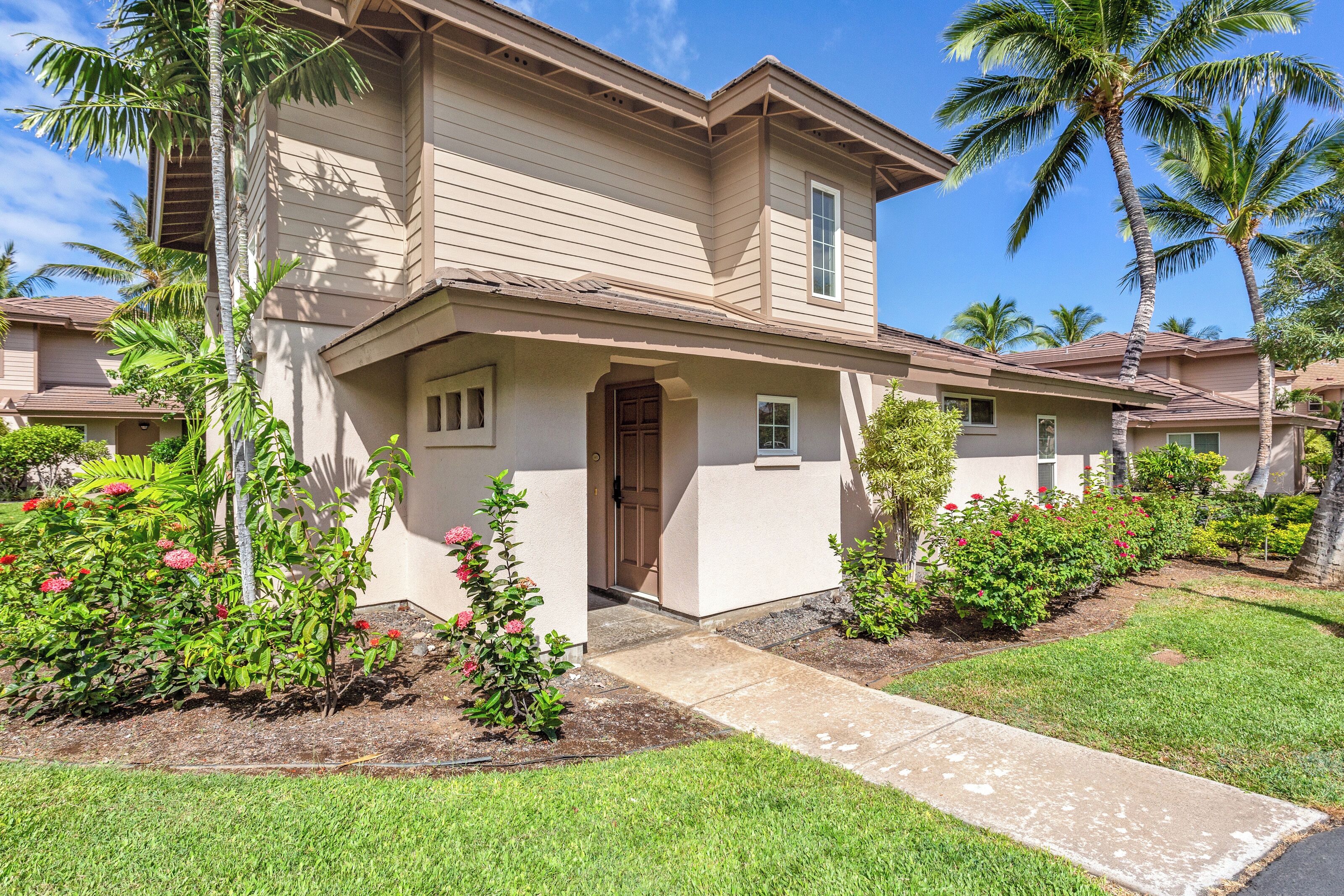 A two-story house with a front porch, palm trees, and a well-maintained garden.