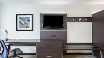 A modern hotel room with a dark wood desk, a flat-screen TV, a framed abstract art piece, and a built-in bench.