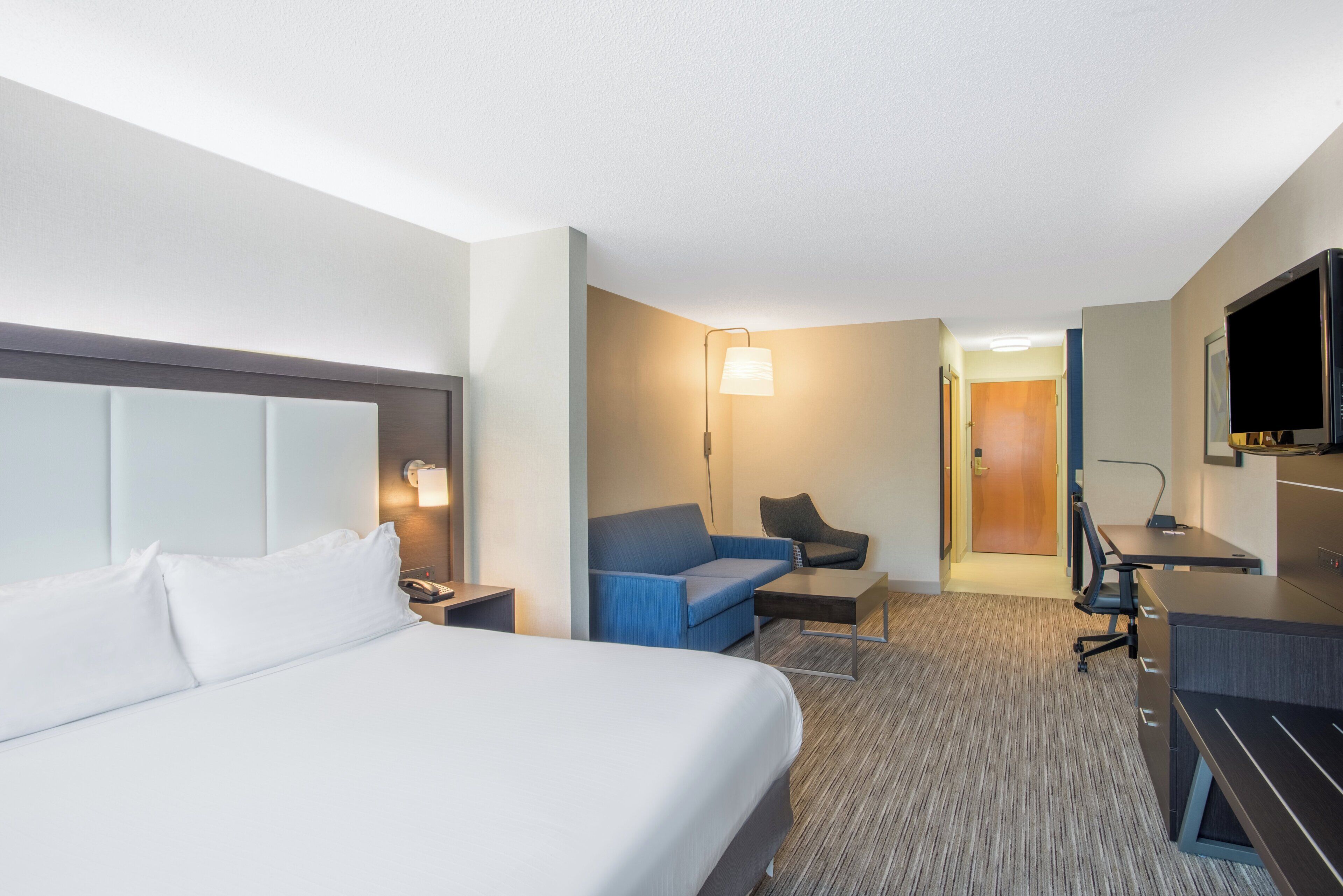 A hotel room with a bed, a desk, a chair, a sofa, and a television.